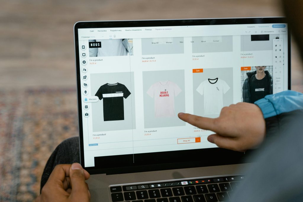 pexels-photo-7667442-7667442 A person points to t-shirt options in an online store on a laptop screen.